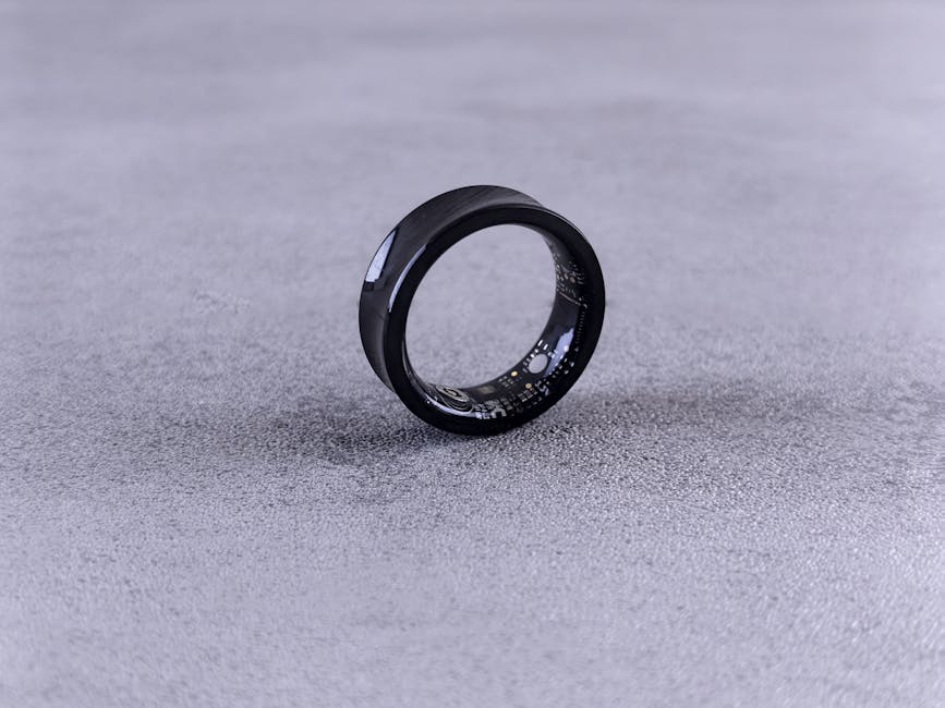 A modern black smart ring with visible circuitry resting on a textured concrete surface.